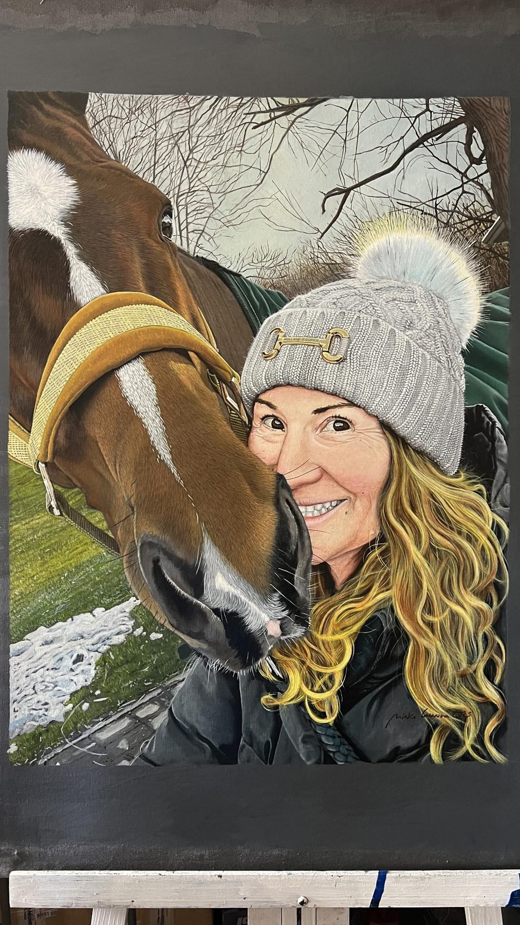 Pintura hiperrealista de una mujer con gorro de lana junto a un caballo alazán