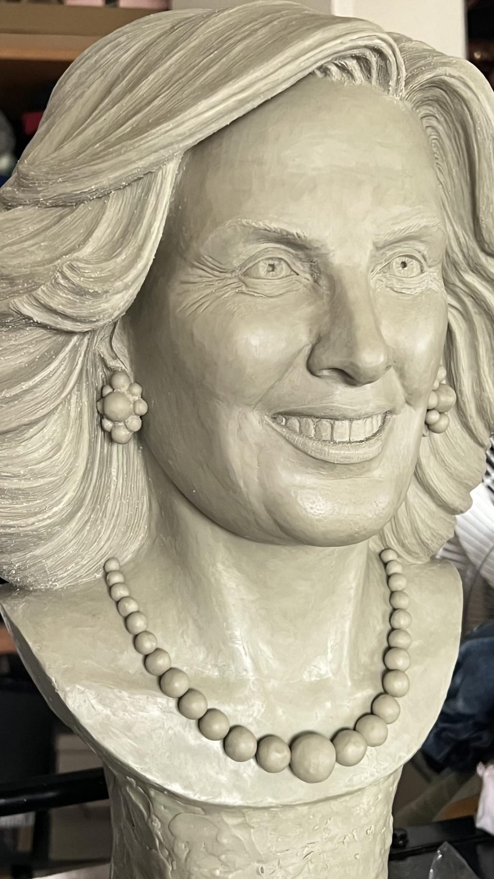 Escultura en arcilla de una mujer sonriente con aros y collar de perlas